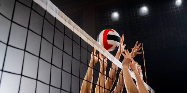 Women volleyball players hands blocking volleyball ball during match at night.